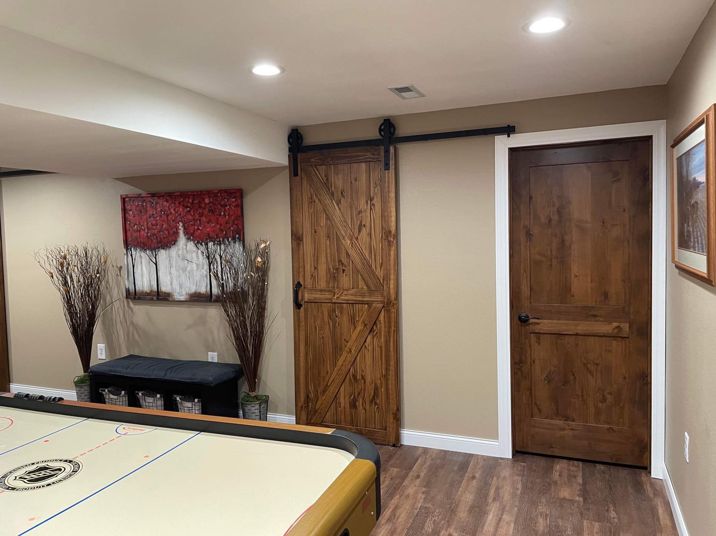 Wood sliding barn door and matching hinged door with white trim in a finished basement