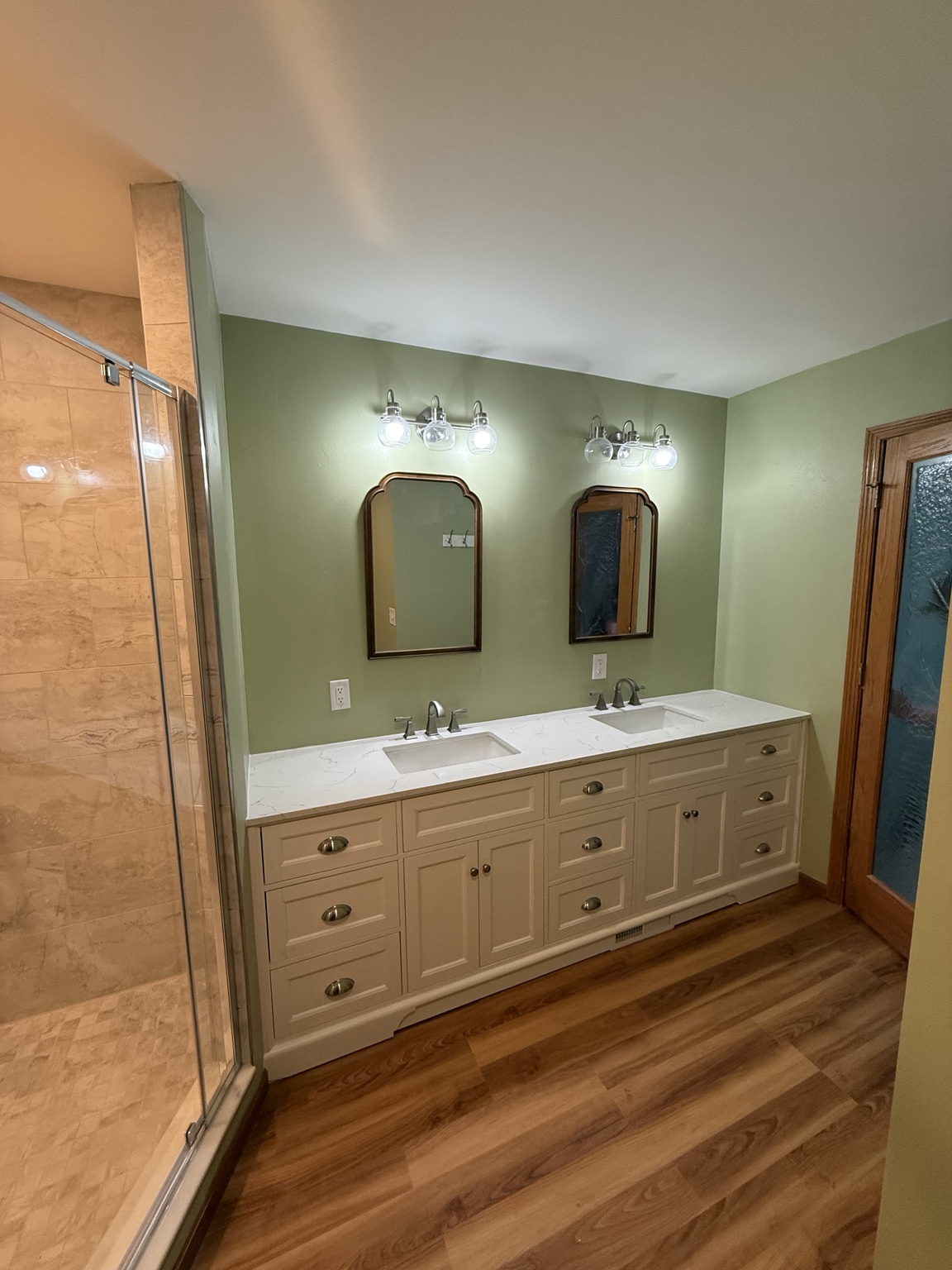 Bathroom with double vanity, twin mirrors, green walls, and wood-look flooring