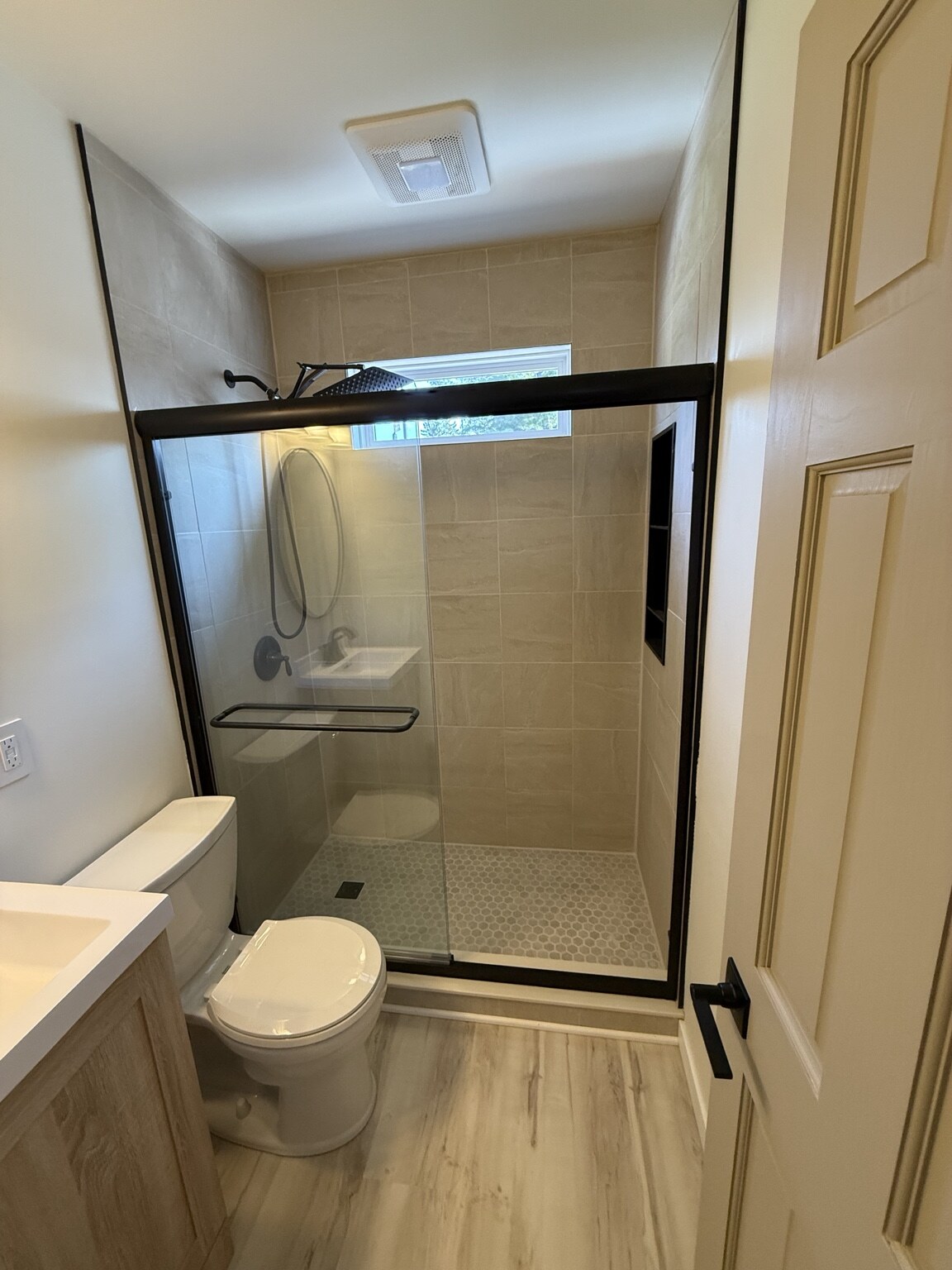 Compact bathroom with tiled glass shower, light vanity, and coordinated flooring