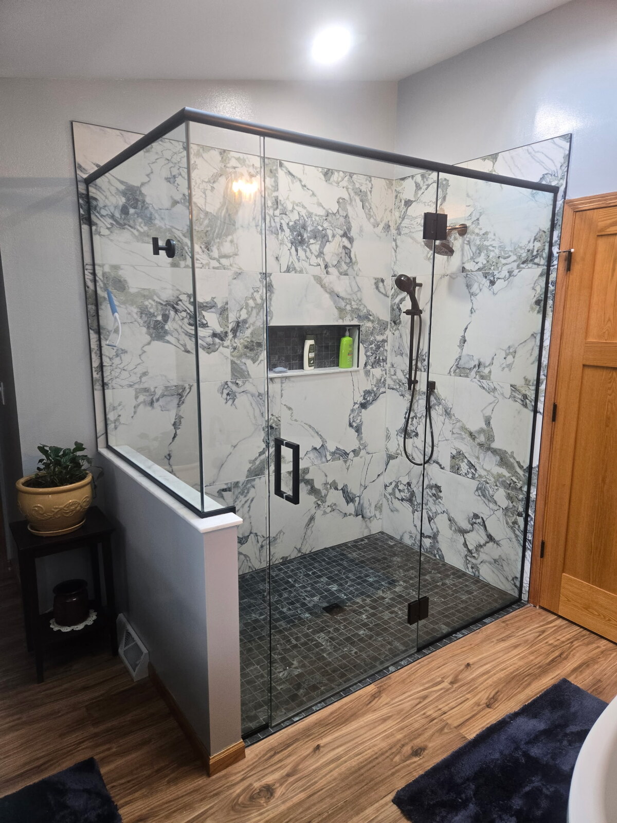 Custom glass shower with marble-look tile and dark fixtures
