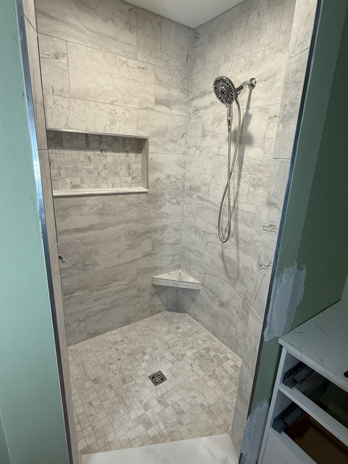 Tiled shower with a recessed wall niche, corner shelf, and handheld shower fixture