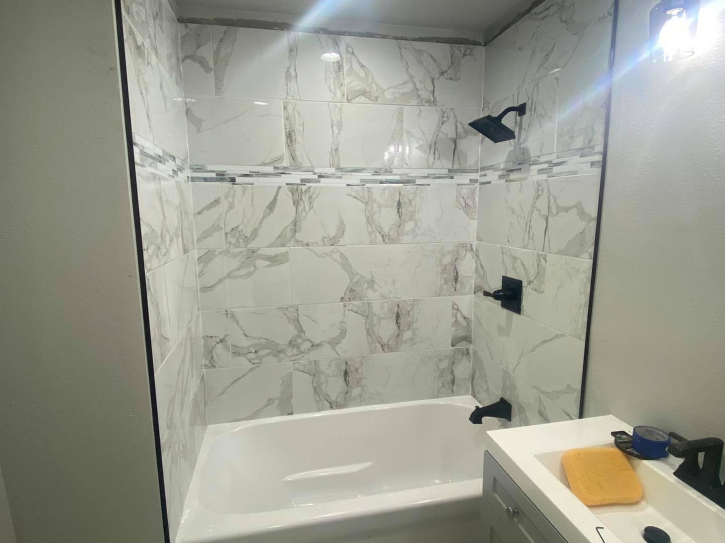White bathtub with marble-look wall tile, a mosaic accent band, and dark shower fixtures