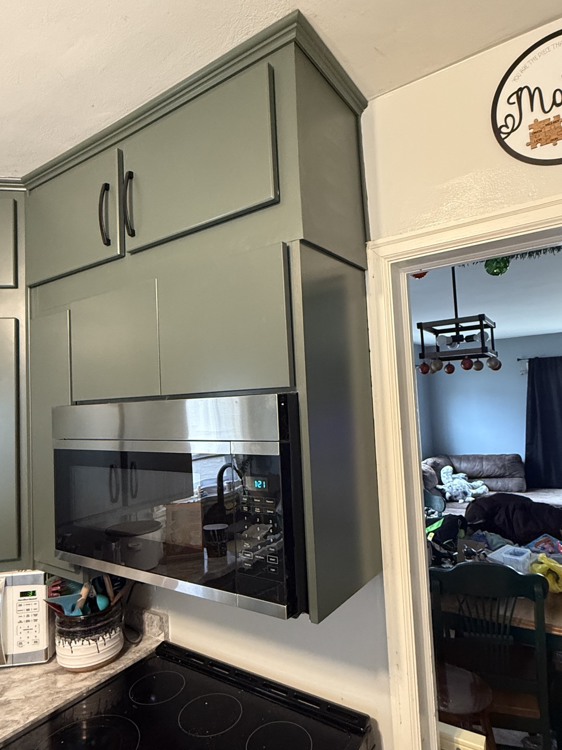 Green kitchen cabinets surrounding a stainless microwave with finished upper trim