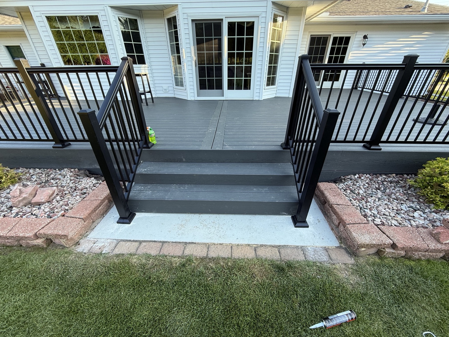 Gray composite deck with wide steps and dark metal railings at a home entrance