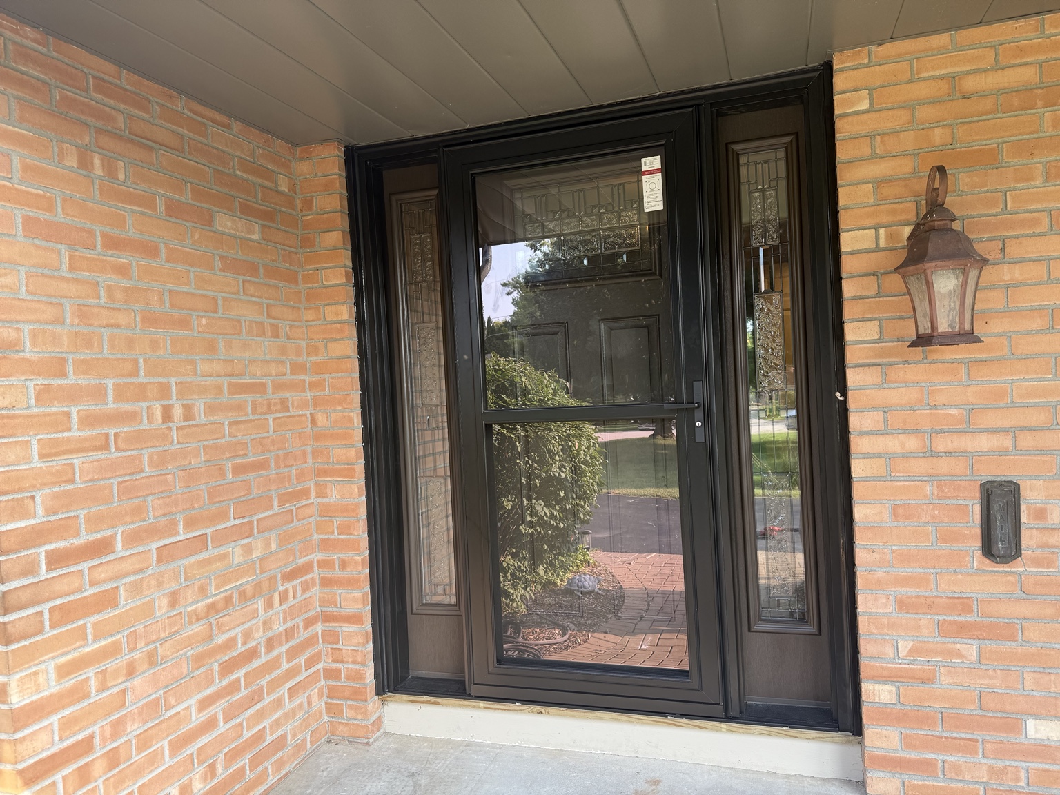 Exterior view of a dark entry door with a glass storm door and decorative sidelights in a brick entrance