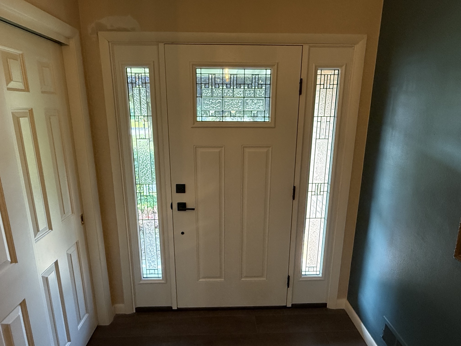 Interior view of a white entry door with decorative glass, matching sidelights, and white trim