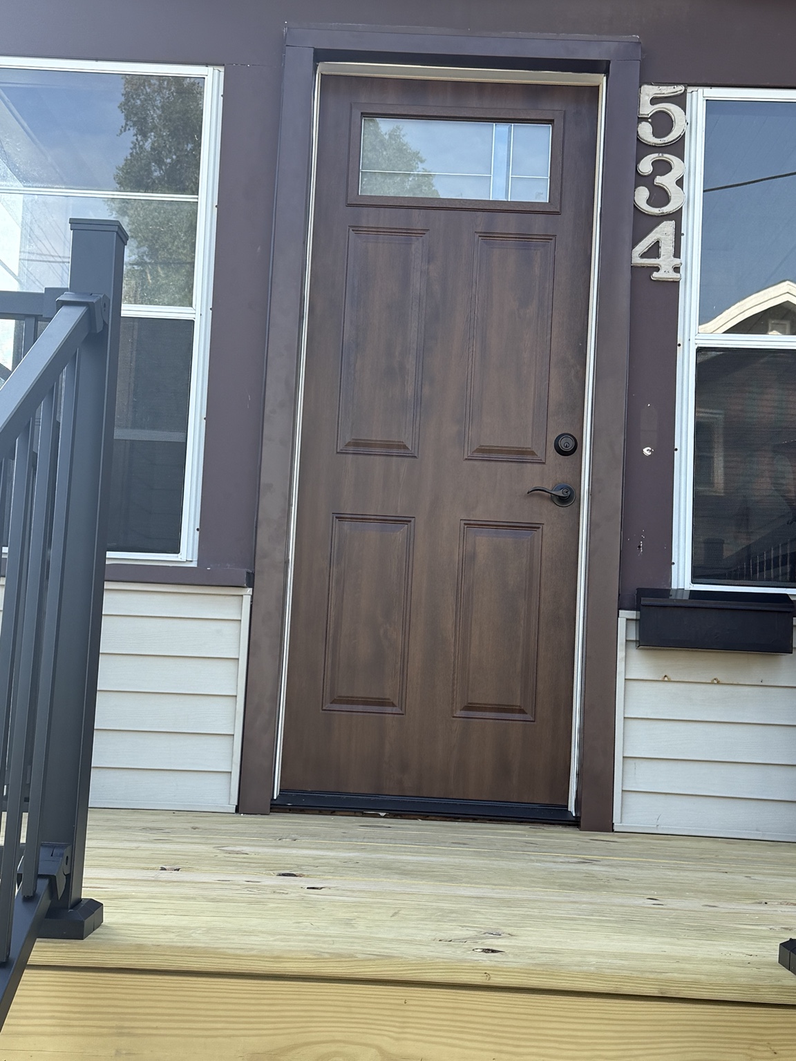 Wood-look exterior entry door with an upper glass panel, dark hardware, and a wood porch