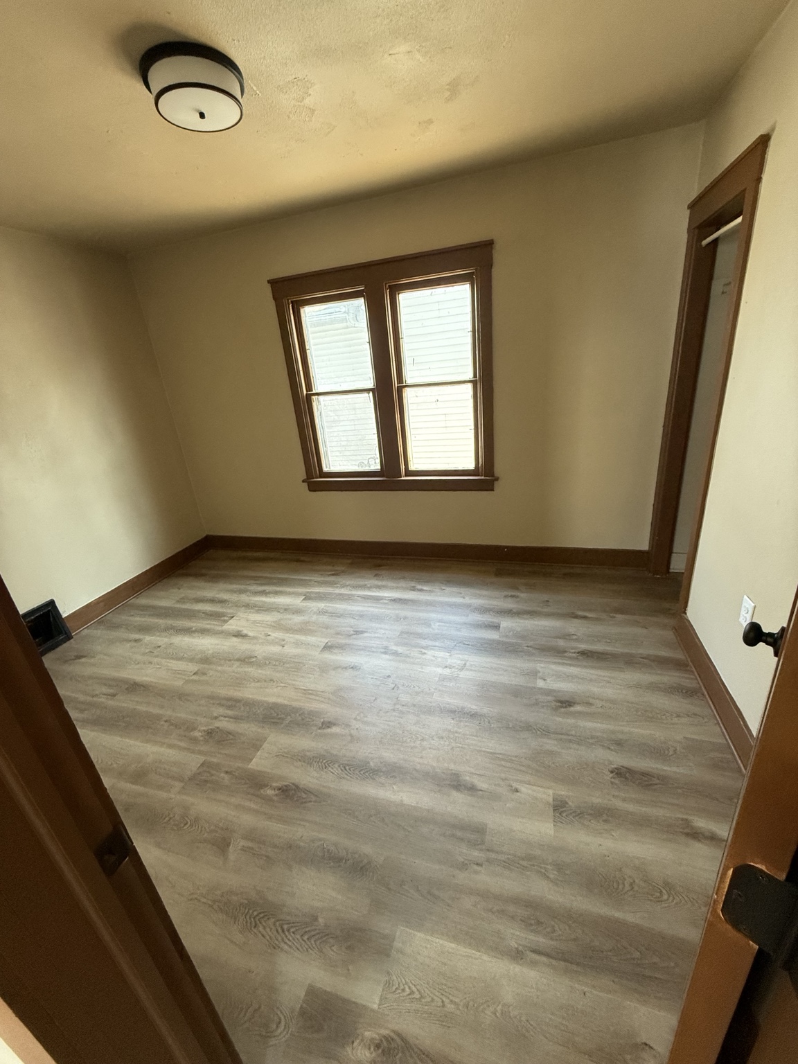 Room with gray wood-look flooring and wood trim around the window and baseboards