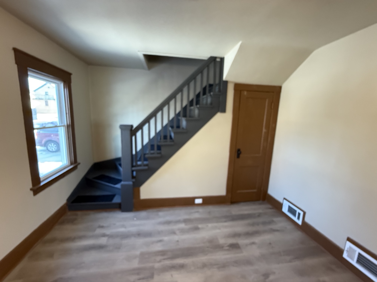 Finished room with gray wood-look flooring, wood window trim, and a dark staircase