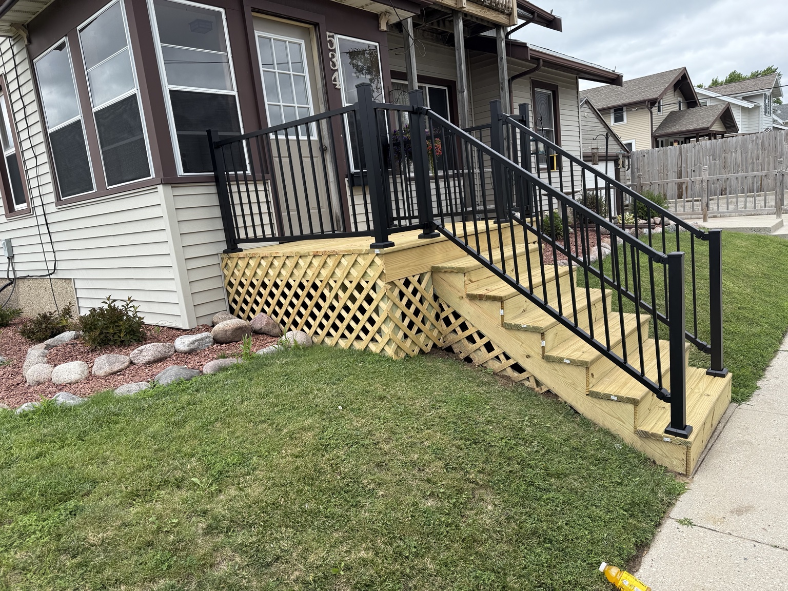Raised wood porch with wide wood steps, black metal railings, and lattice skirting