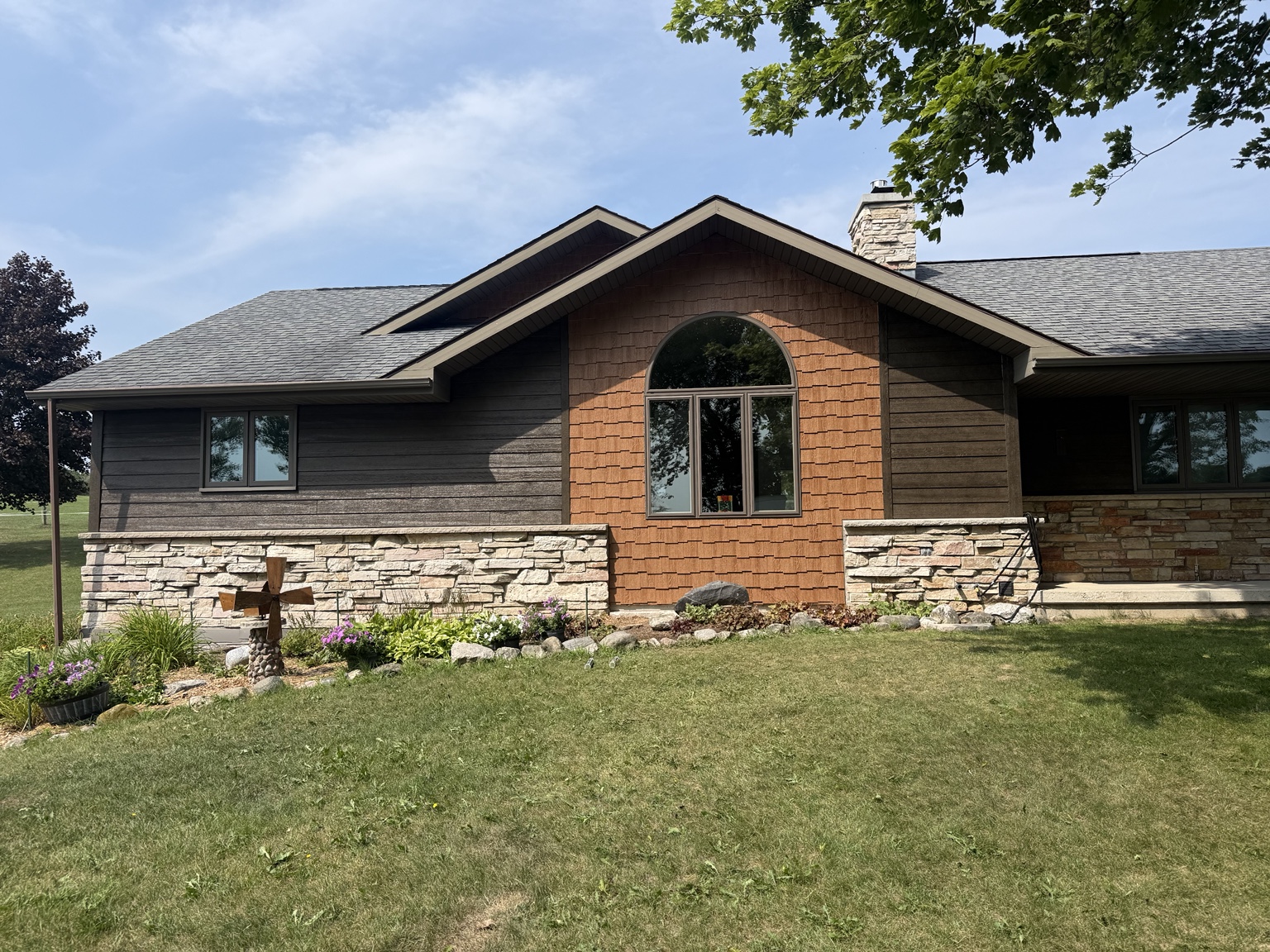 Home exterior with dark horizontal siding, warm shake-style accent siding, coordinated trim, and stone lower walls