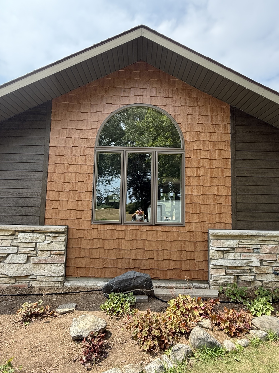 Close view of warm shake-style siding around an arched window, with dark horizontal siding and stone accents