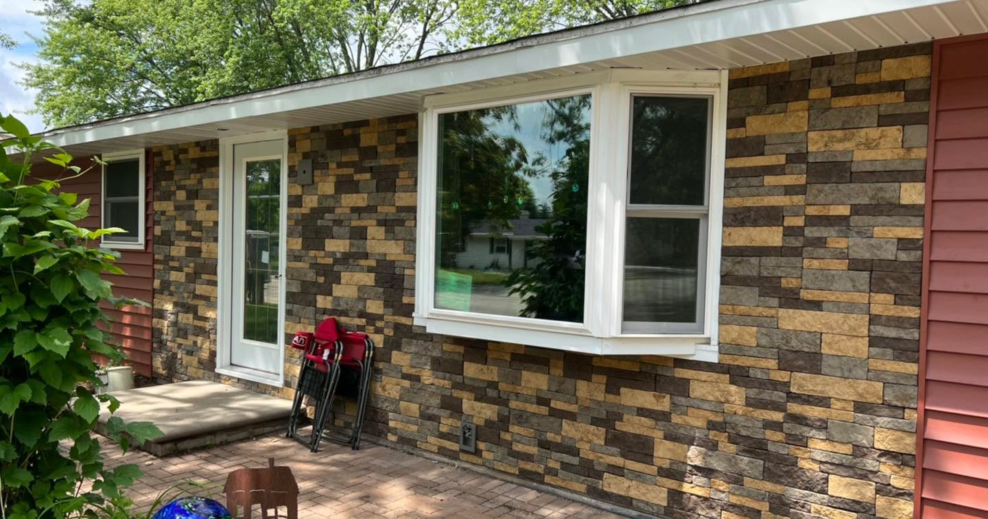 Home exterior with stone-look cladding around a white bay window and entry door alongside red siding