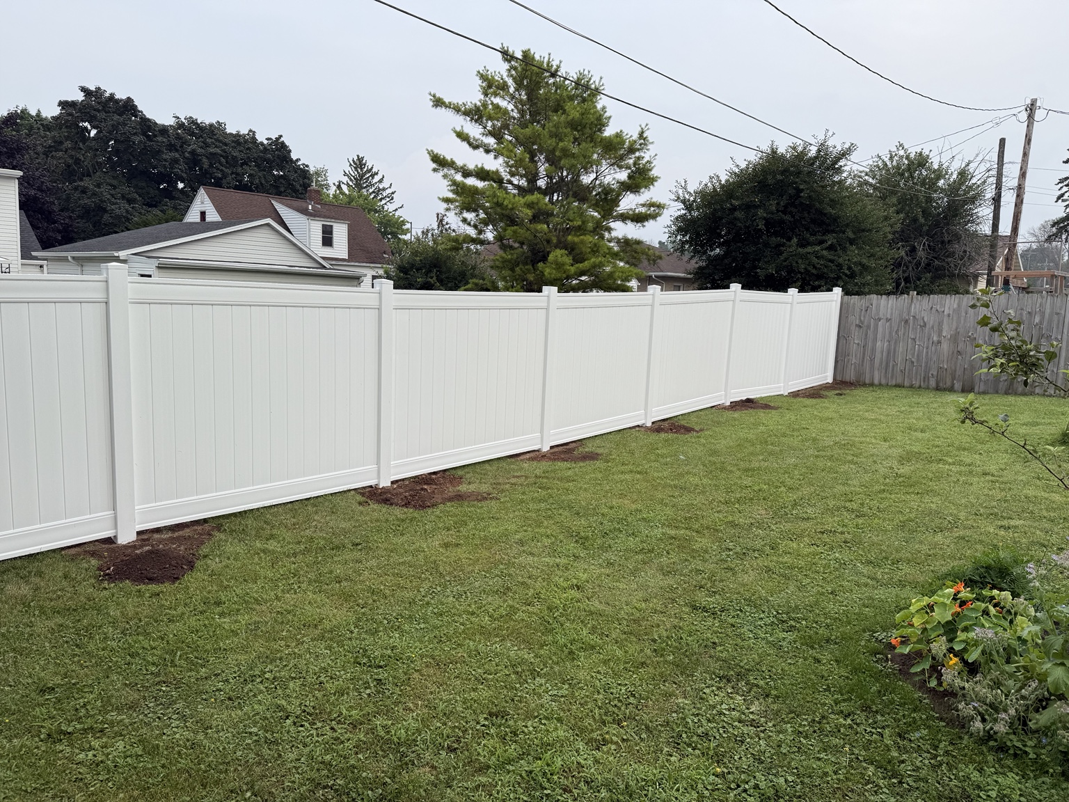 Long white vinyl privacy fence along a green backyard