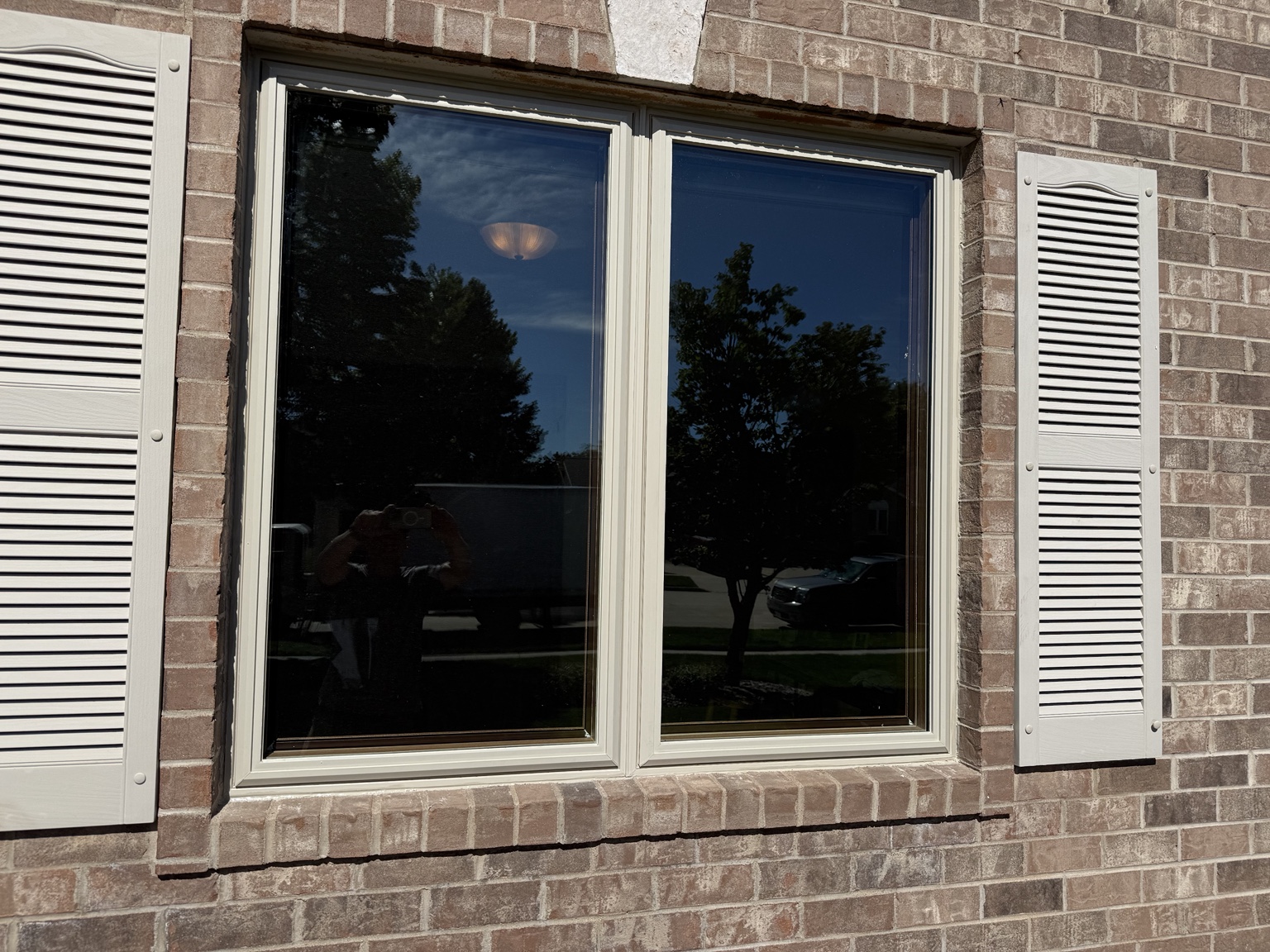 Exterior view of a twin window installation in a brick home with light-colored trim and shutters